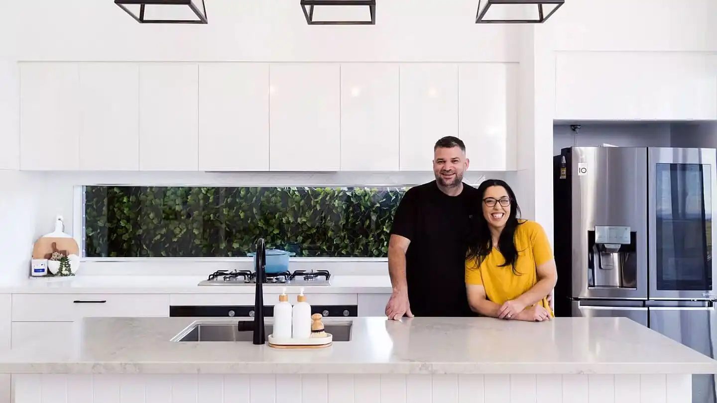 Interior photo of a couple smiling in their open-concept kitchen.