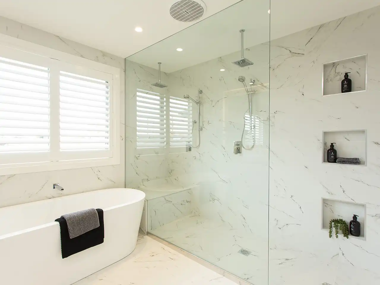 Photo of a bathroom with dual shower heads and freestanding bath, with the walls and floors covered in white, marble-textured tiling as part of the Simonds Castlemaine 41 home design