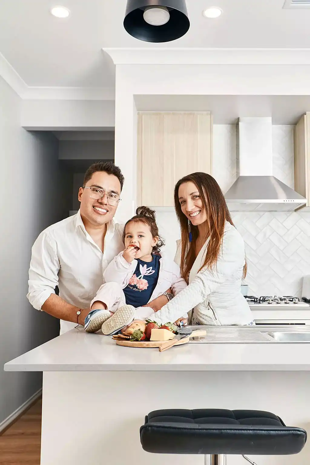 This image features a young family in a open-concept kitchen space with wooden floors.