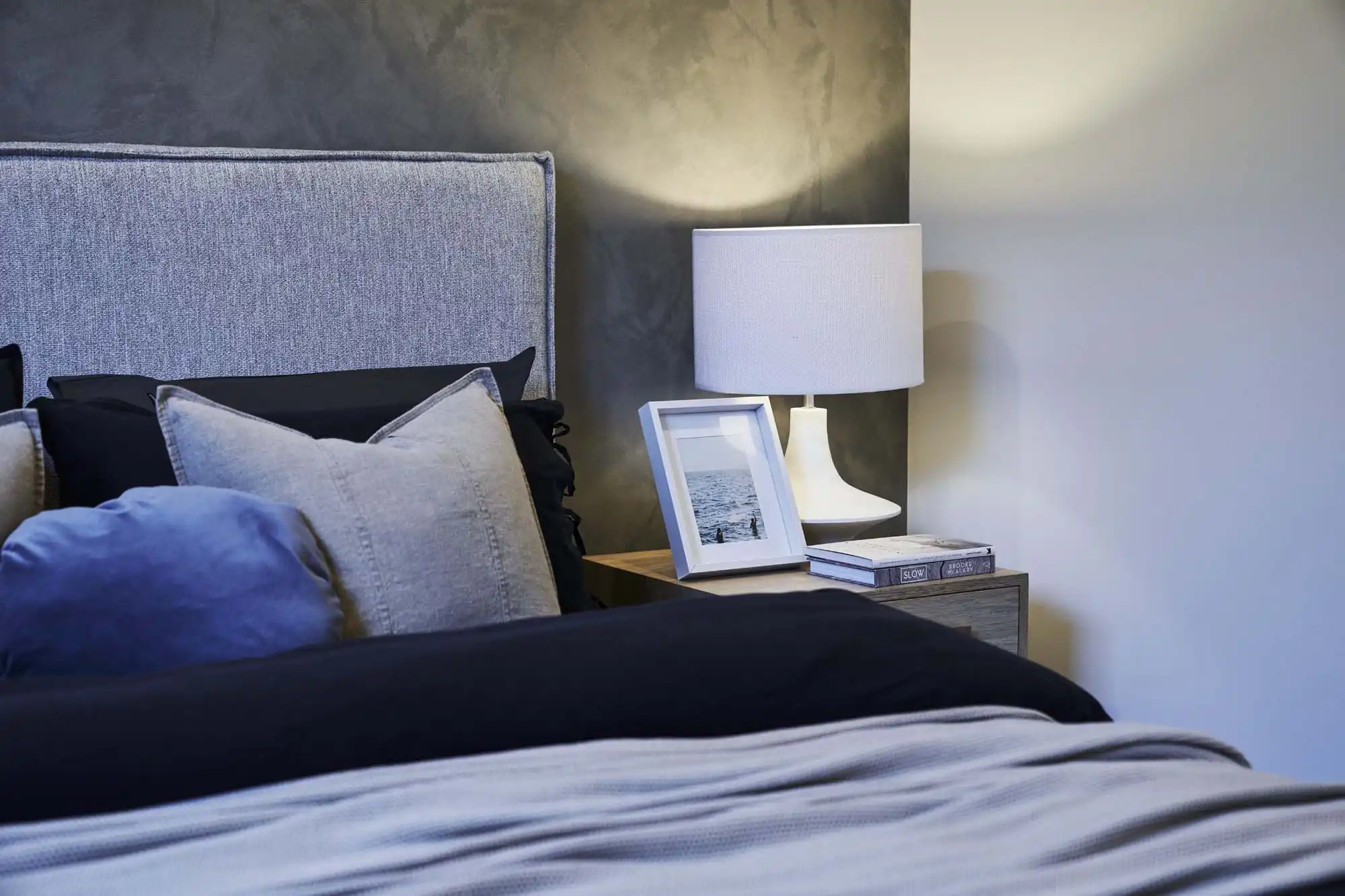 Close up photo of the right side of a bed with dark and moody colours, next a wooden bed-side table, in the Simonds Lomandra 42 home design