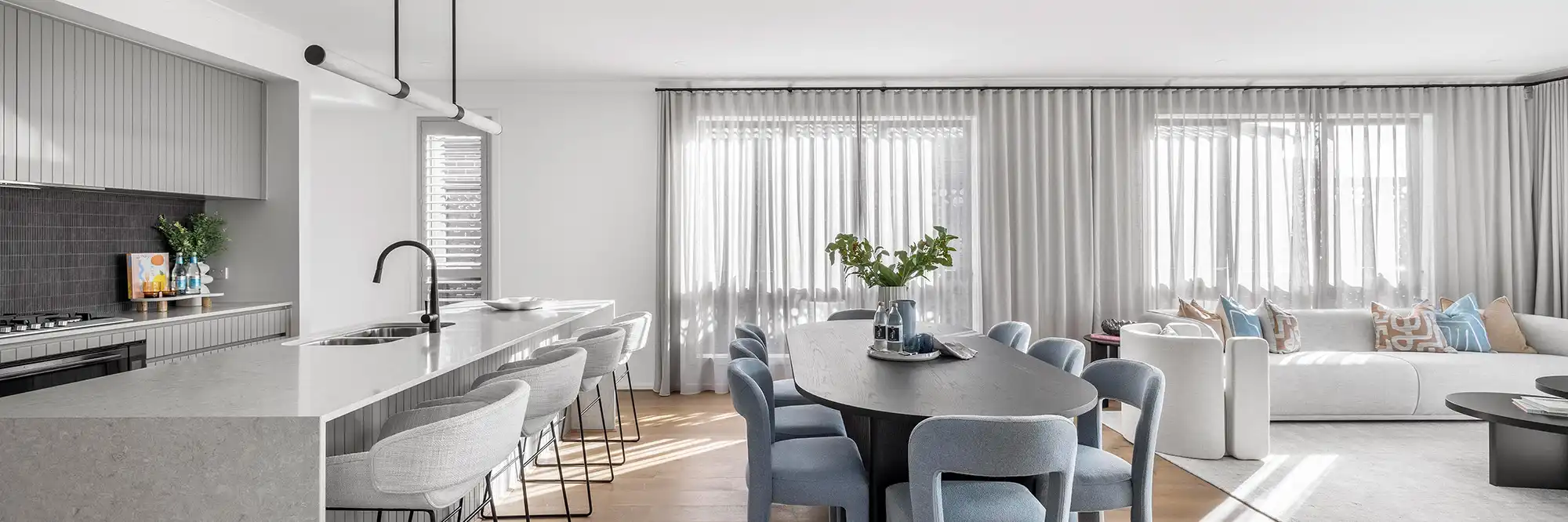 Interior photo of a modern home kitchen and living space, featuring a light grey stone benchtop and a dark grey splashback kitchen tiling, as seen in the Simonds single storey Fairlight 27 modern home design