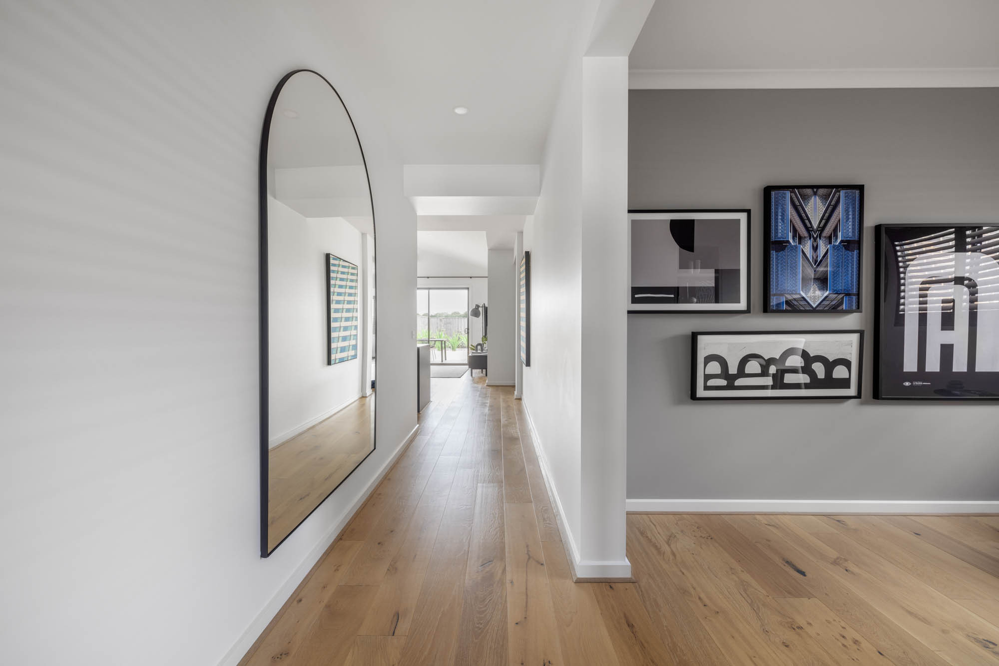 An interior image of a living area with framed photographs, a hallway with a large mirror and wooden floors as a part of Simonds Berrima home design..