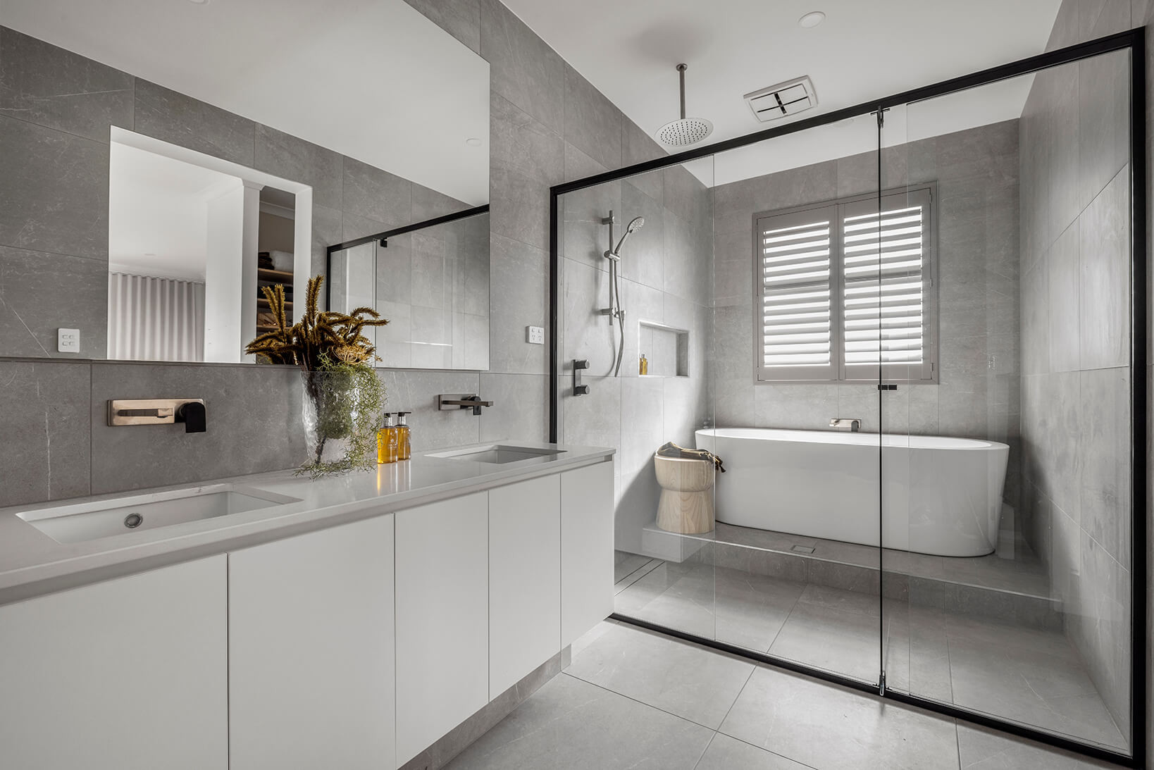 Photo of a modern bathroom surrounded in grey stone tiles and a double sink basin next to a glass screen door that divides the basin from a shower and freestanding bathtub in the Simonds South Australia Hampstead 32 home design
