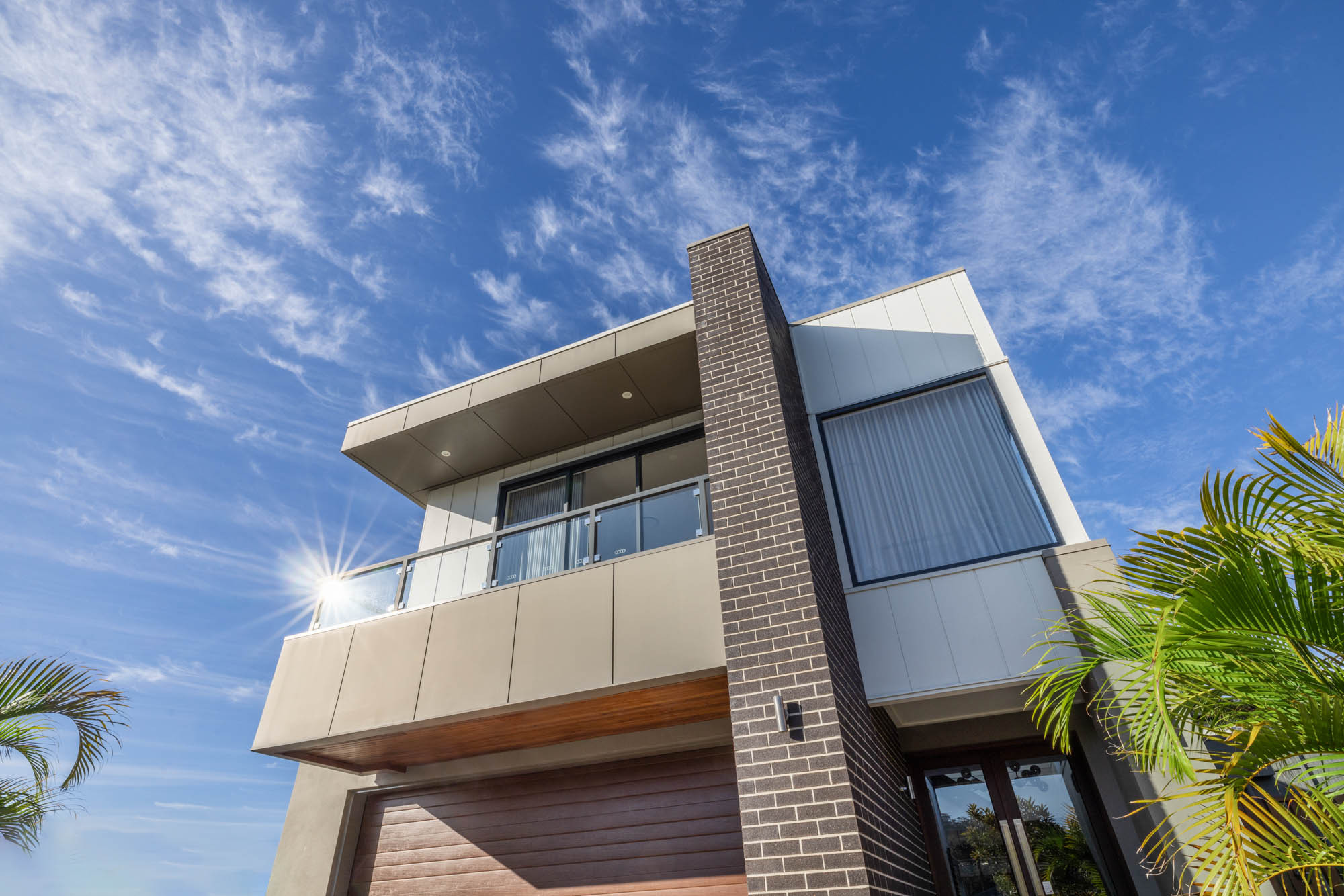 An exterior image of a double storey home with a balcony and large sliding windows and a garage space as a part of Colston 26 home design.