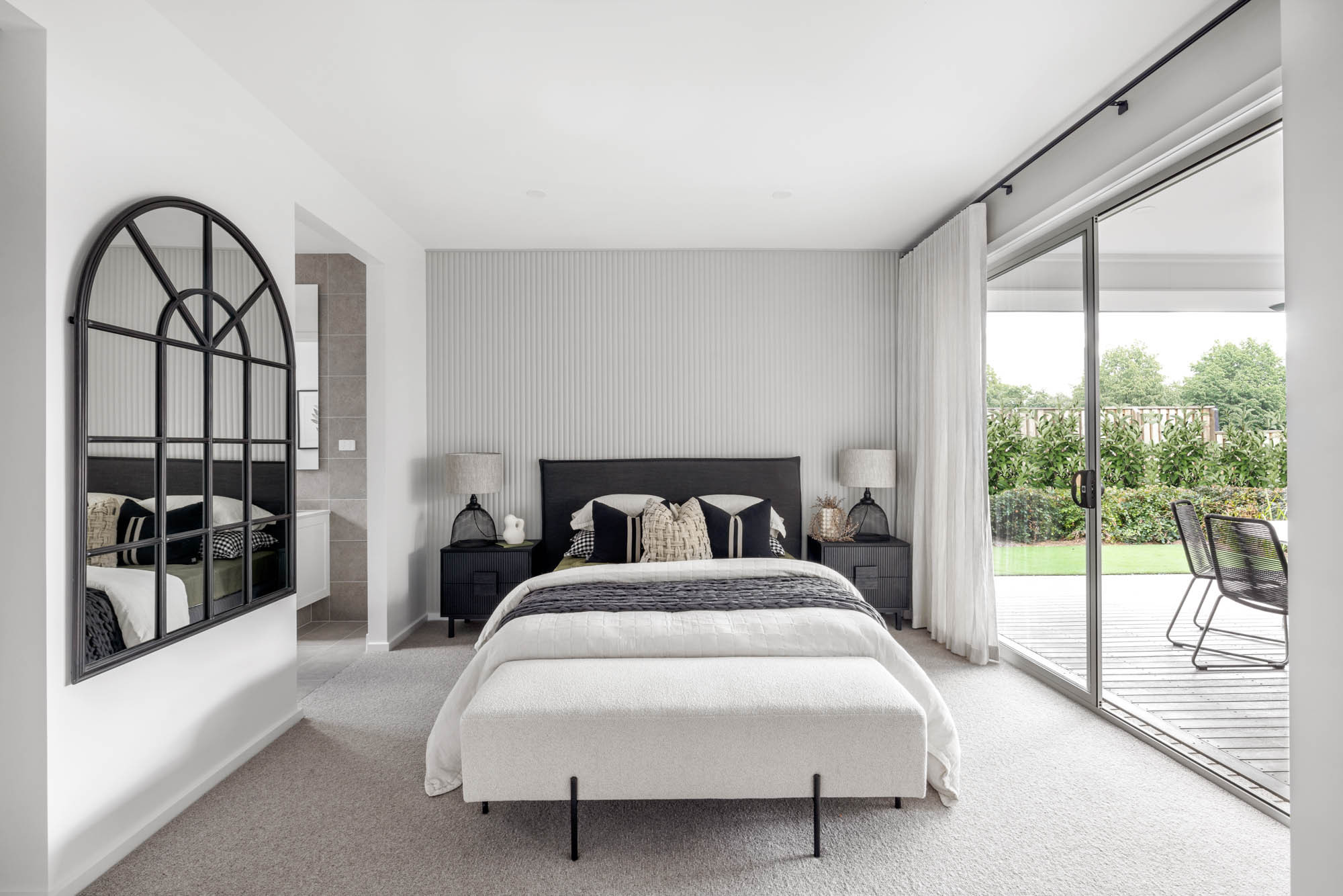 Photo of a guest bedroom with light grey panelled feature wall, to the left is the ensuite, to the right is a slider door that connects to the outdoor alfresco area, providing plenty of natural lighting to the guest bedroom, all apart of the Simonds Queensland Riverway 26 home design