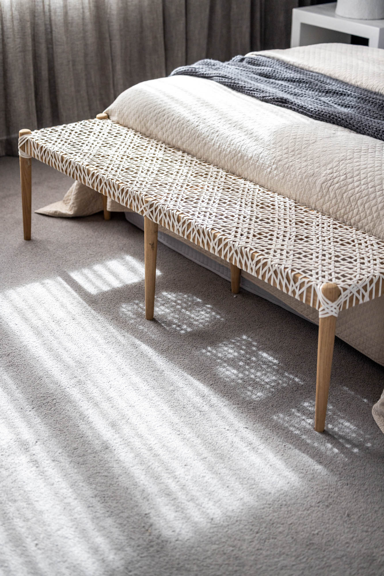 Photo that is focusing on the end of a bed and the light grey carpet below it, showing the morning sunlight shining through the window and onto the carpet in a Simonds Travertine 31 home design